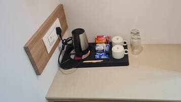 Una kitchenette con cafetera, bolsitas de té, sobres de azúcar y dispensador de agua en la encimera.