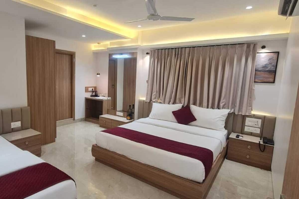A hotel room with two beds, a desk, a vanity, and a ceiling fan.
