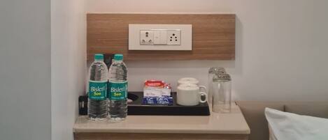 A small bedside table with a water bottle, a coffee maker, and a power outlet.