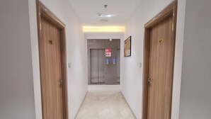 Un couloir avec deux portes en bois, un détecteur d’incendie et un ascenseur.