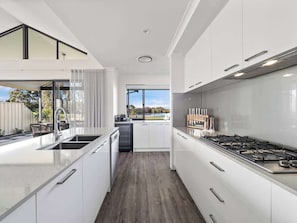 A modern kitchen with white cabinetry, a stainless steel stove, and a large window providing a view of the outdoors.