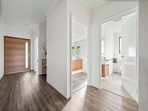 A hallway with wooden flooring, white walls, and a wooden door on the left.