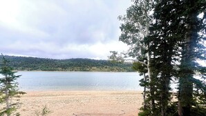 Puinen kävelytie johtaa hiekkarannalle, jonka taustalla on järvi ja metsäisiä kukkuloita.