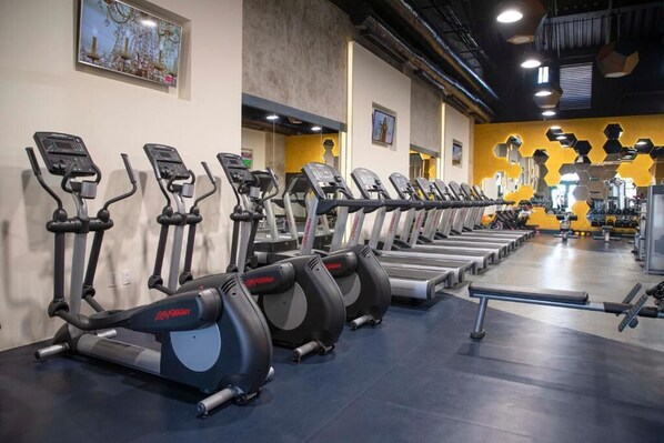 En rad med motionscyklar i ett gym, med en gul vägg och en tv-skärm som är monterad på väggen.