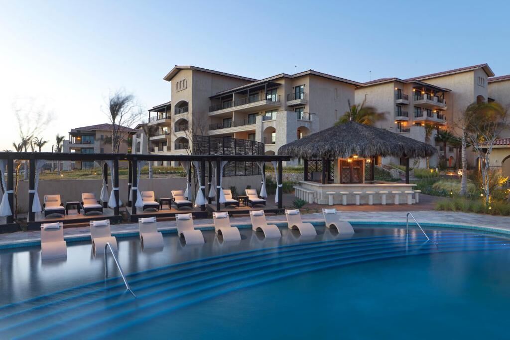 Ein Poolbereich eines Hotels mit Liegestühlen und einer strohgedeckten Struktur.