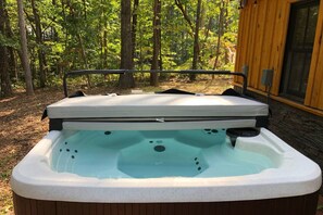 Un jacuzzi con cubierta de madera y baranda metálica, rodeado de árboles.