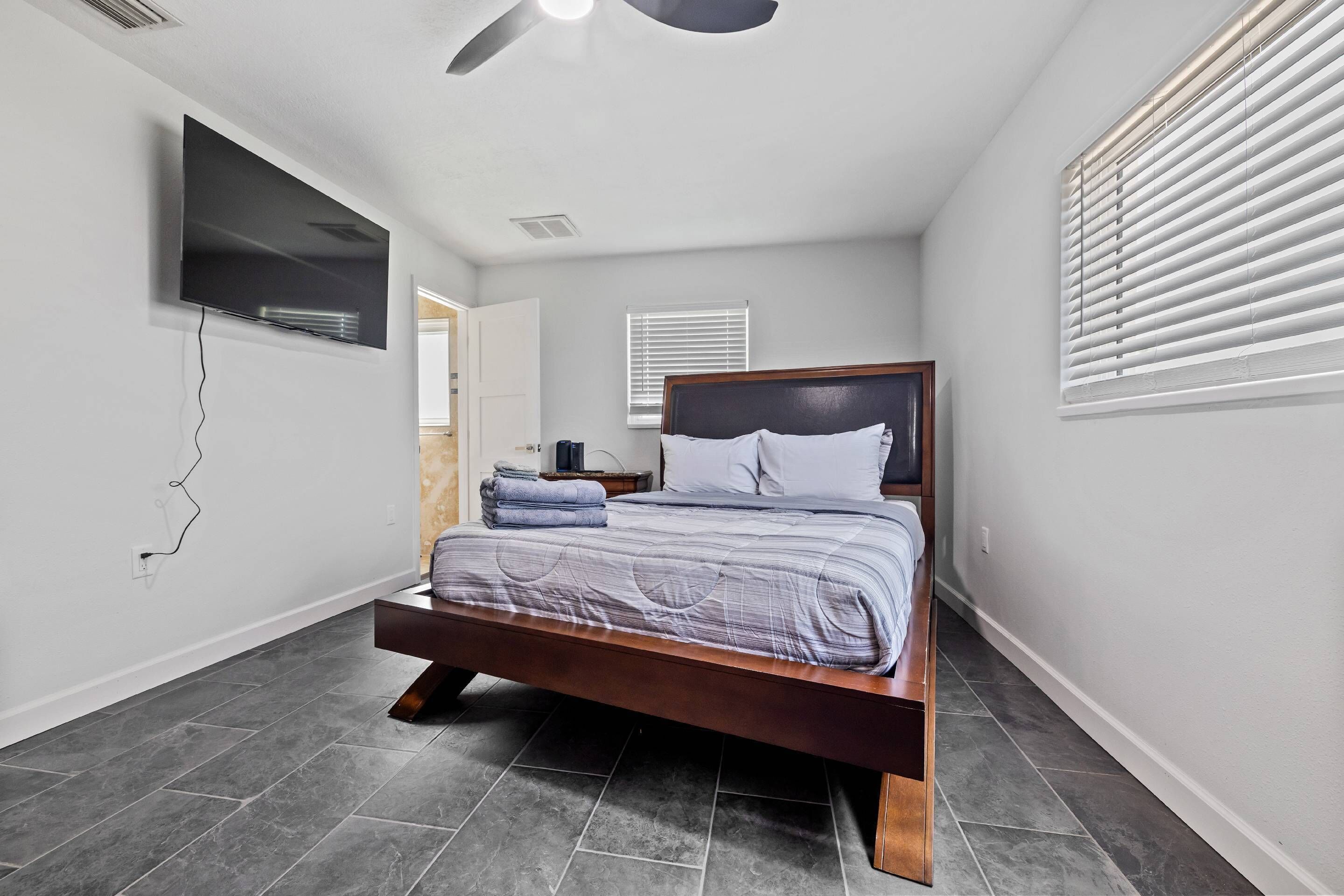 A bedroom with a bed, a TV mounted on the wall, and a ceiling fan.