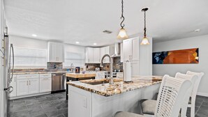 A modern kitchen with white cabinetry, a granite countertop, and a central island with bar seating. - Waterfront with Pool, Ping Pong table, 3 Kayaks, Fishing Pier, Private Access to the Gulf (Port Richey)