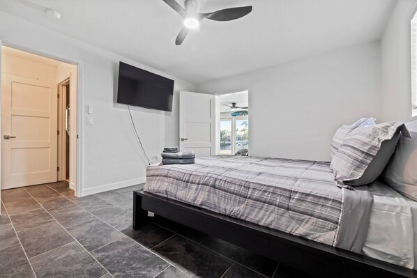 A bedroom with a bed, a ceiling fan, a TV, and a door leading to another room. - Waterfront with Pool, Ping Pong table, 3 Kayaks, Fishing Pier, Private Access to the Gulf (Port Richey)