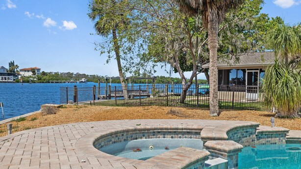 A swimming pool with a curved design, surrounded by a brick deck and a fence. - Waterfront with Pool, Ping Pong table, 3 Kayaks, Fishing Pier, Private Access to the Gulf (Port Richey)