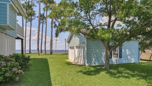 A small, light blue wooden structure with a white door, surrounded by a well-maintained lawn and tall trees, with a body of water in the background. - Riverfront Aurora Home w/ Deck & Private Pier! (Aurora)