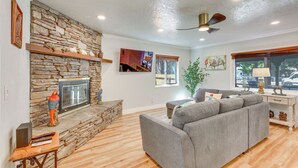 Un salon avec une cheminée en pierre, un canapé gris et un ventilateur de plafond.