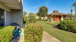 A residential building with a red door, a covered patio with outdoor furniture, and well-maintained lawns.