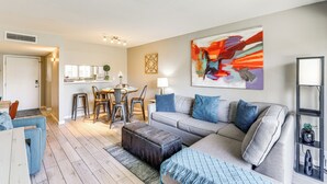 A modern living room with a grey sofa, blue cushions, a coffee table, and a dining area with a table and chairs.