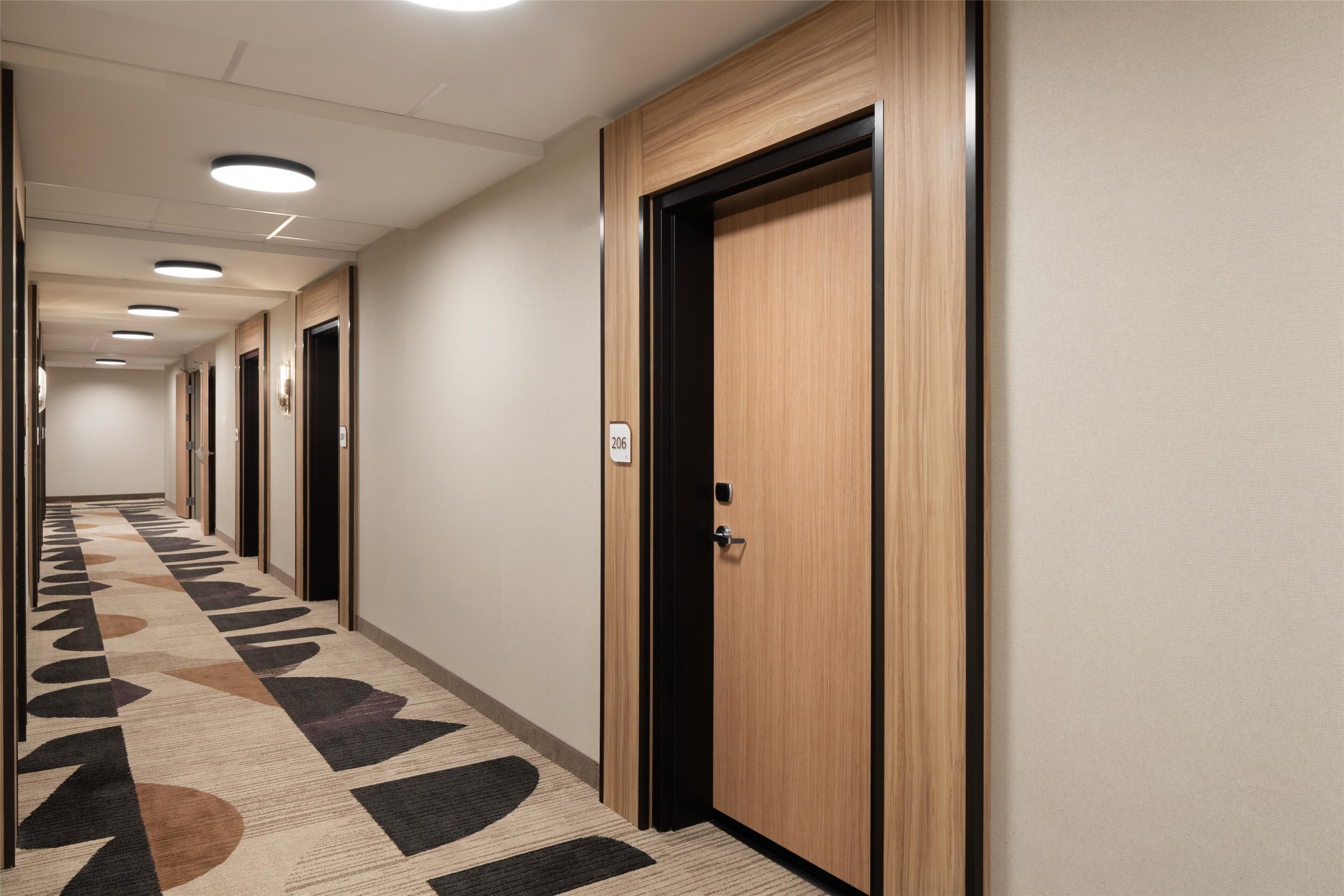 A hotel hallway with multiple doors, a patterned carpet, and recessed ceiling lights.