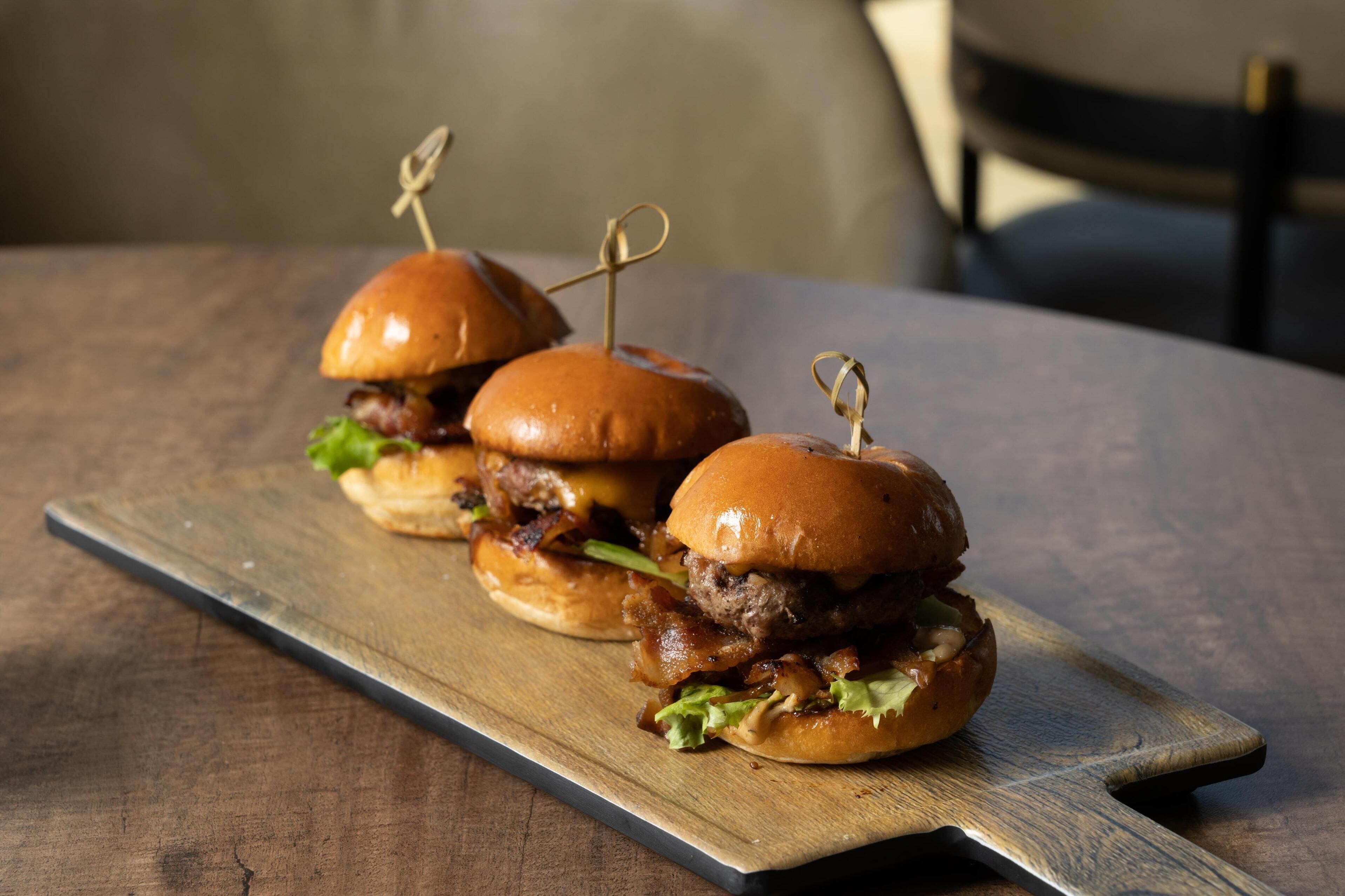 Three burgers on a wooden board.