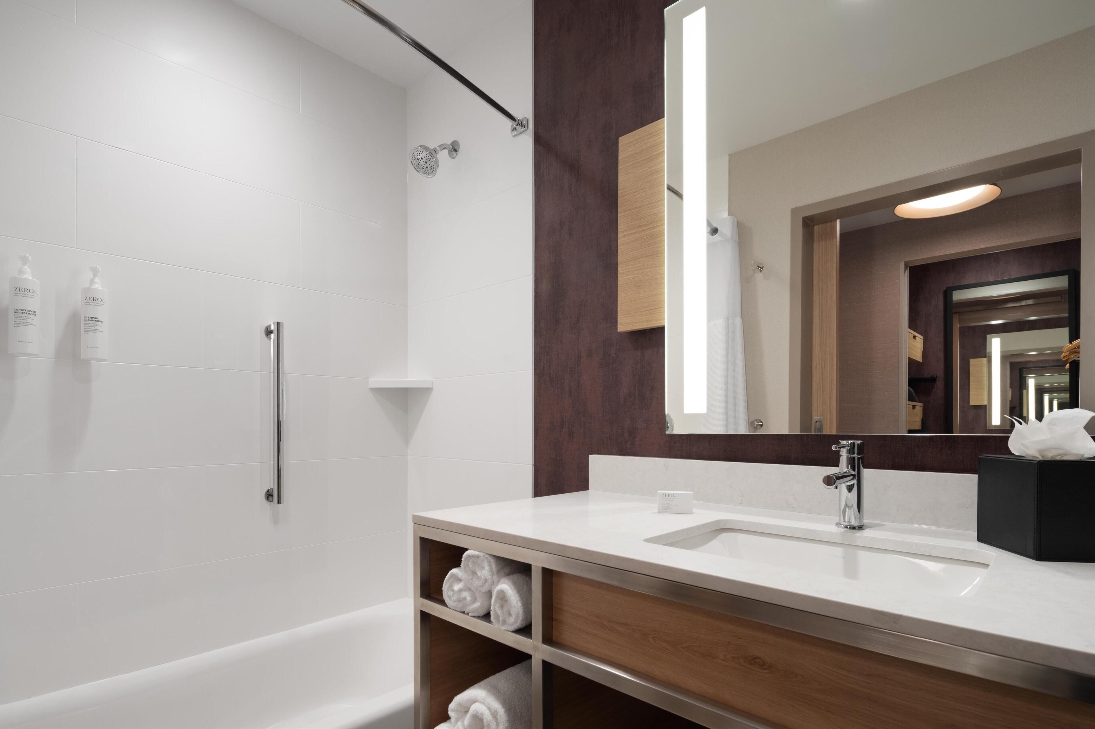 A modern bathroom with a white sink, a large mirror, and a shower.