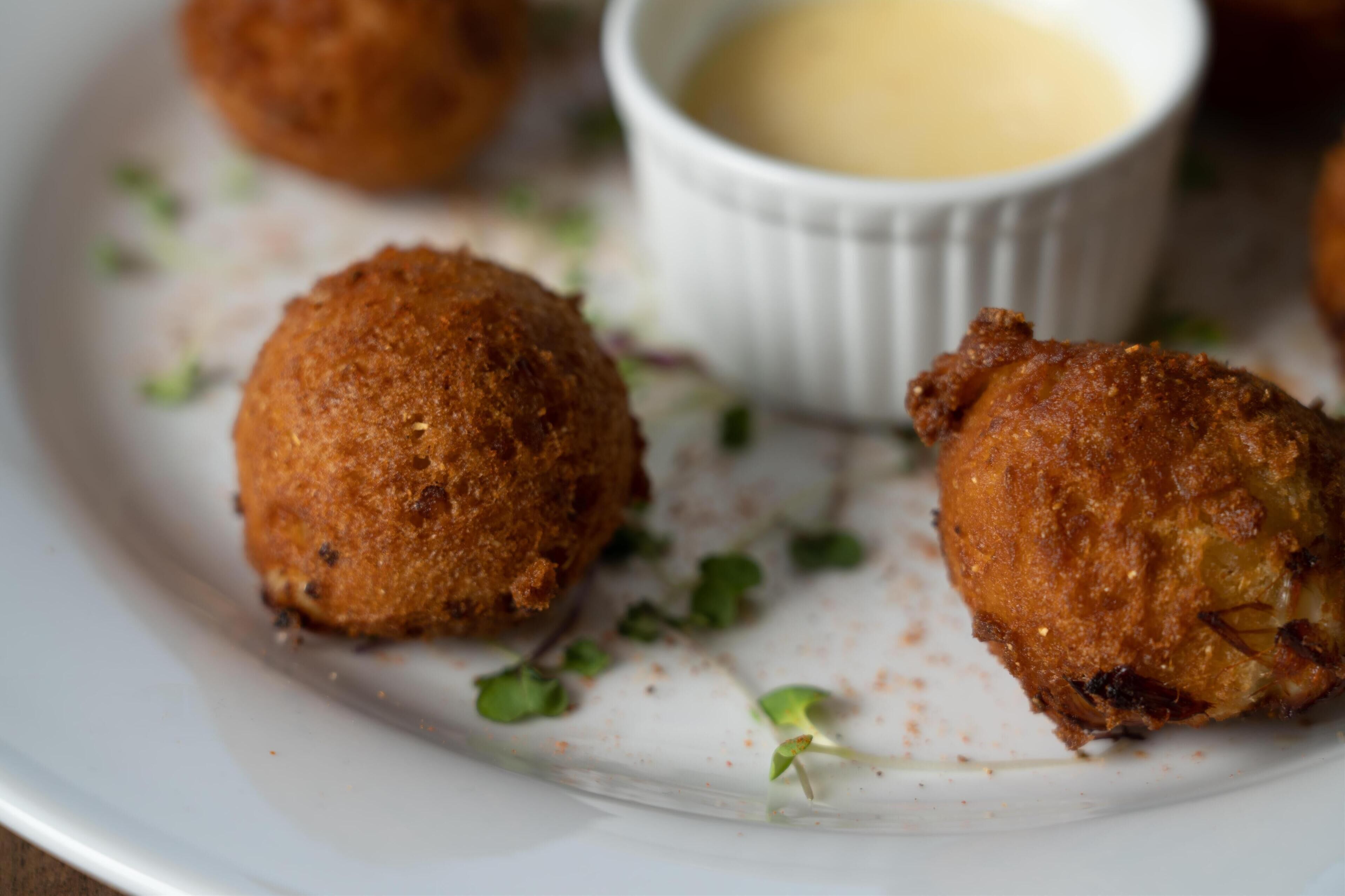 A plate with three golden-brown croquettes and a small bowl of dipping sauce.
