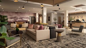 A modern hotel lobby with a sofa, armchairs, a coffee table, and a reception desk. - Hilton Garden INN Greenville University (Greenville)