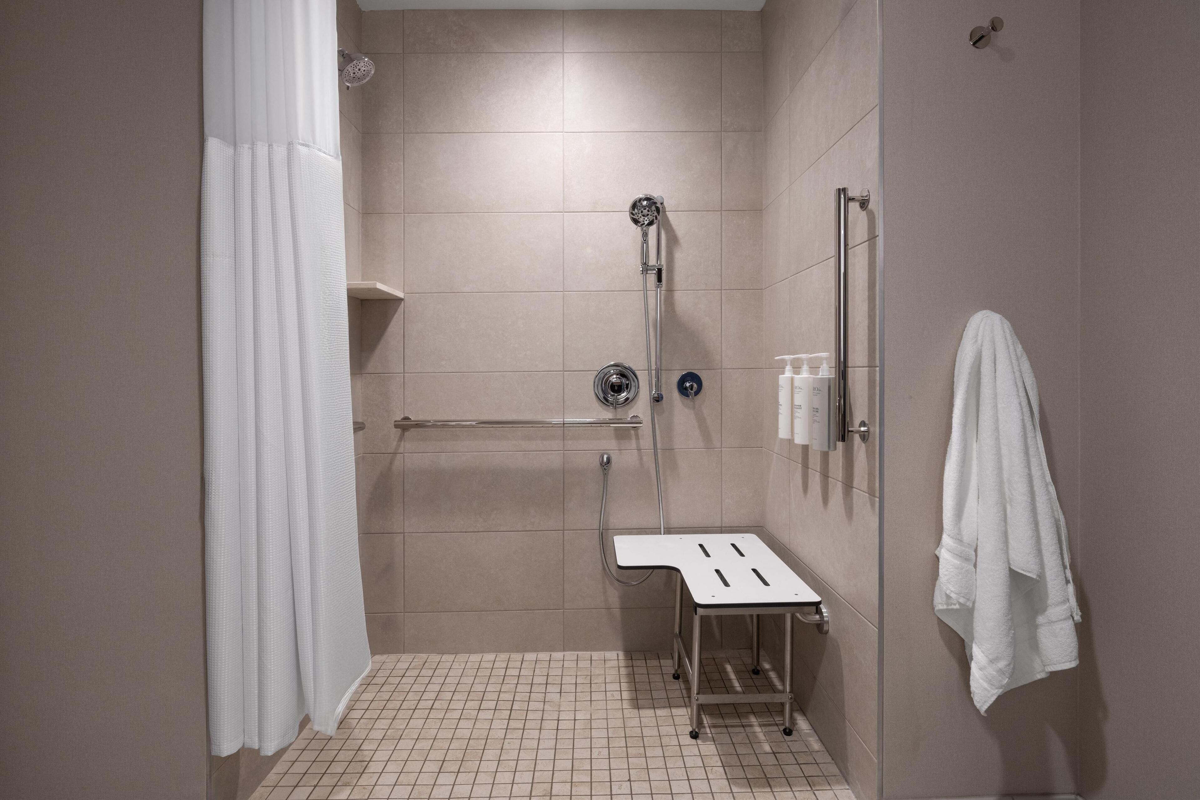 A modern shower area with a handheld showerhead, a handheld shower attachment, and a small stool.