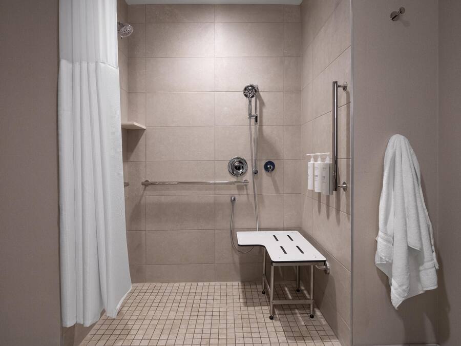 A modern shower area with a handheld showerhead, a handheld shower attachment, and a small stool.