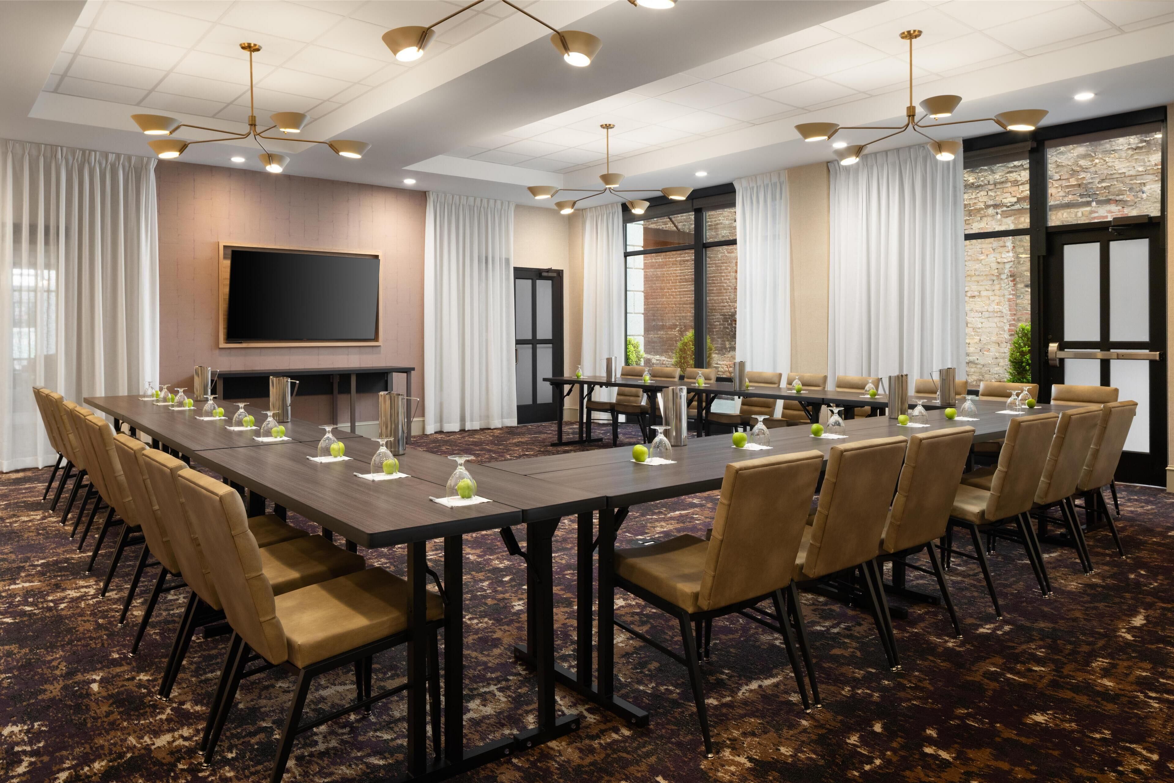 A conference room with a long table, chairs, a flat-screen TV, and a brick wall.