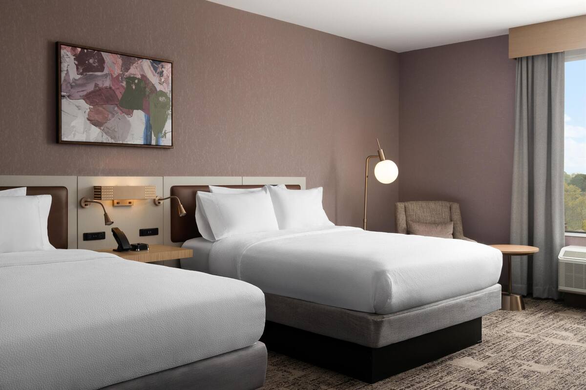 Une chambre d’hôtel avec deux lits, un bureau, une chaise, une lampe et un tableau au mur.