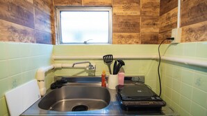 A kitchen with a stainless steel sink, a window above the sink, and wooden wall tiles. - Chateau Yoyogi 1-401 (Tokyo)