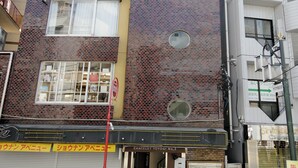 A multi-story building with a brick facade, multiple windows, and a visible storefront at the ground level. - Chateau Yoyogi 1-401 (Tokyo)