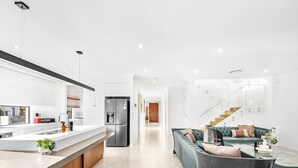 Eine moderne Küche mit einer zentralen Kochinsel, ein Essbereich mit einer Couch und Stühlen sowie eine Treppe zu einer oberen Ebene.