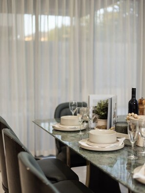 A dining table set with plates, glasses, and a bottle, with a chair and a plant in the background.
