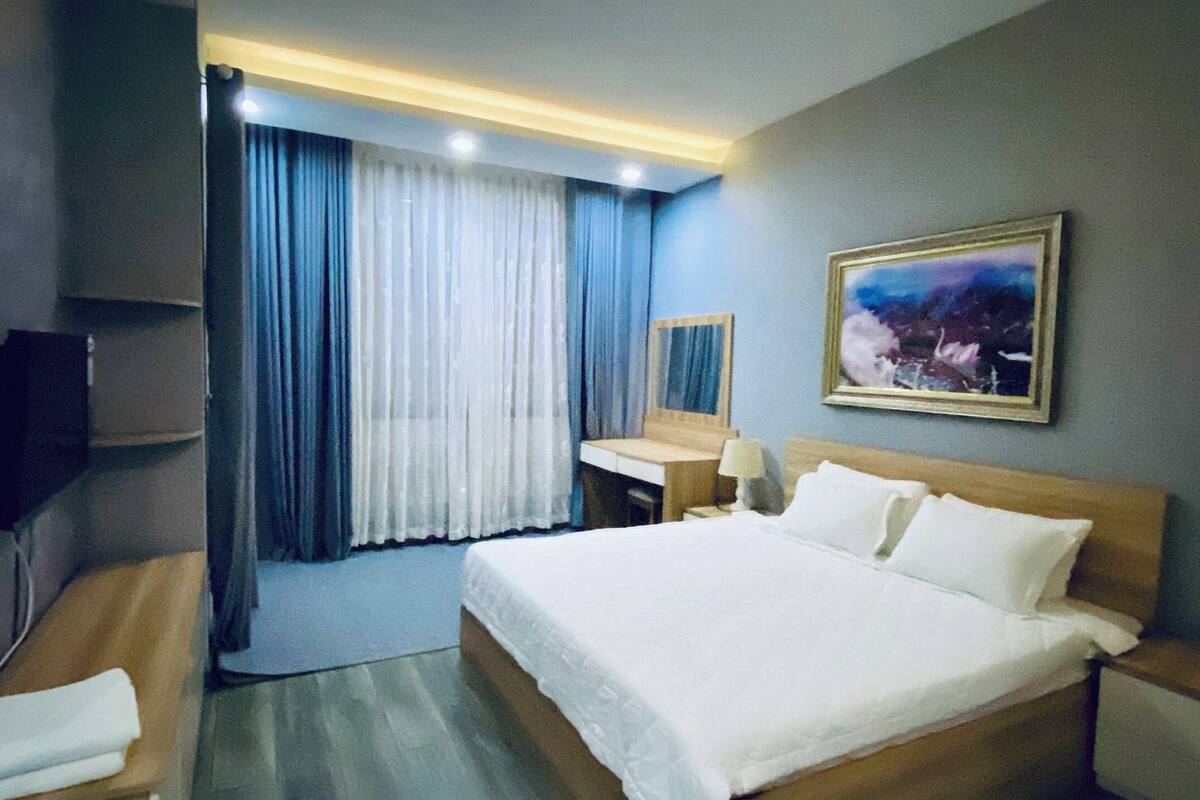 A hotel room with a large bed, a desk, a chair, a TV, and a painting on the wall.