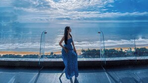A woman in a blue dress standing on a balcony overlooking a beach with a clear sky. - Oasky Vung Tau (Ho Chi Minh City)