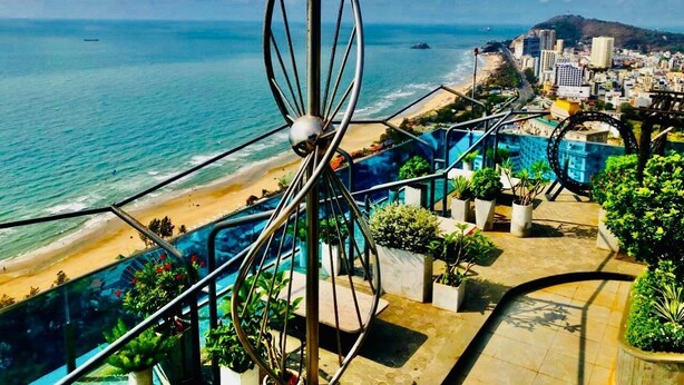 A coastal cityscape with a beach, buildings, and a distinctive metal sculpture. - Oasky Vung Tau (Ho Chi Minh City)