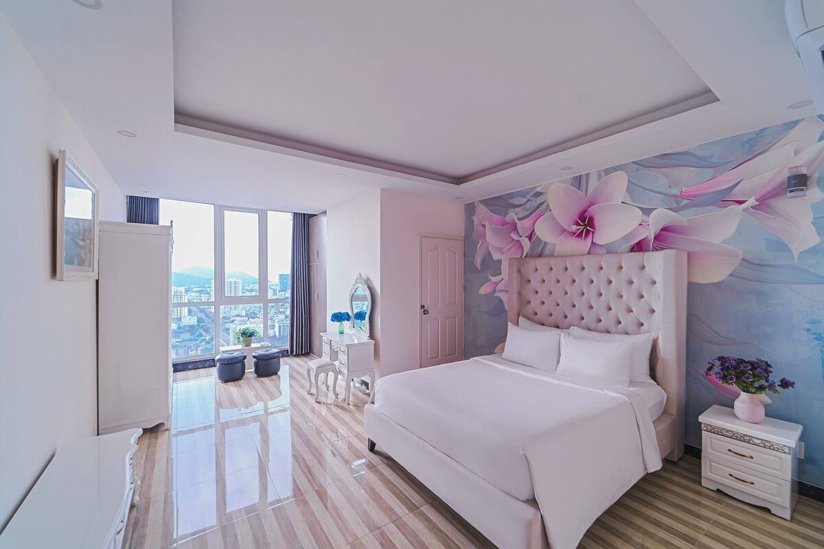A modern bedroom with a large bed, a vanity with a mirror, and a view of the city through large windows.