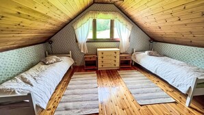 Ein gemütliches Schlafzimmer im Dachgeschoss mit zwei Einzelbetten, einer Holzkommode und einem Fenster mit Vorhängen.
