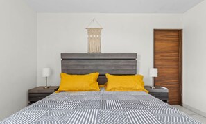 Ein Schlafzimmer mit einem Bett, zwei Nachttischlampen, einer Holztür und einem Wandbehang aus Makramee.