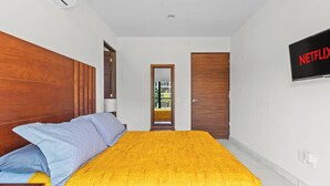 A bedroom with a bed, a wooden headboard, a TV mounted on the wall, and a door leading to another room.