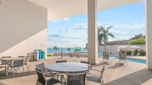 An outdoor seating area with tables and chairs, a pool, and a view of the ocean.