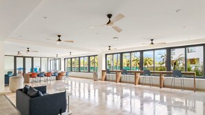 A spacious, well-lit room with large windows, ceiling fans, and a mix of seating arrangements including a sofa and chairs.