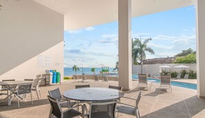 A covered outdoor area with a pool, lounge chairs, and a view of the ocean.