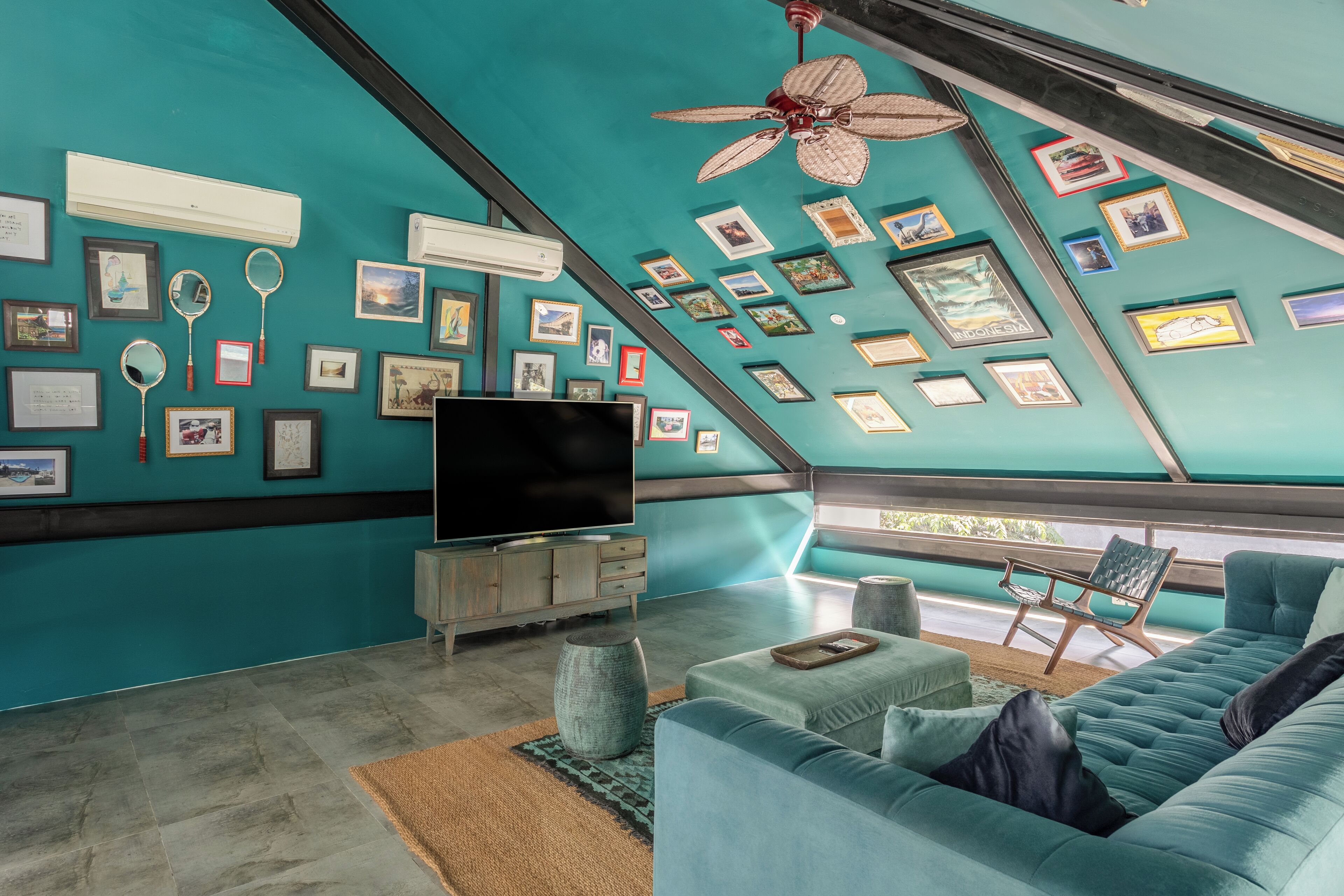A modern living room with a large TV, teal walls, and numerous framed pictures.