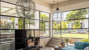 A spacious living room with a large sofa, a television, and two hanging light fixtures. - Smeralda Villa (Canggu)