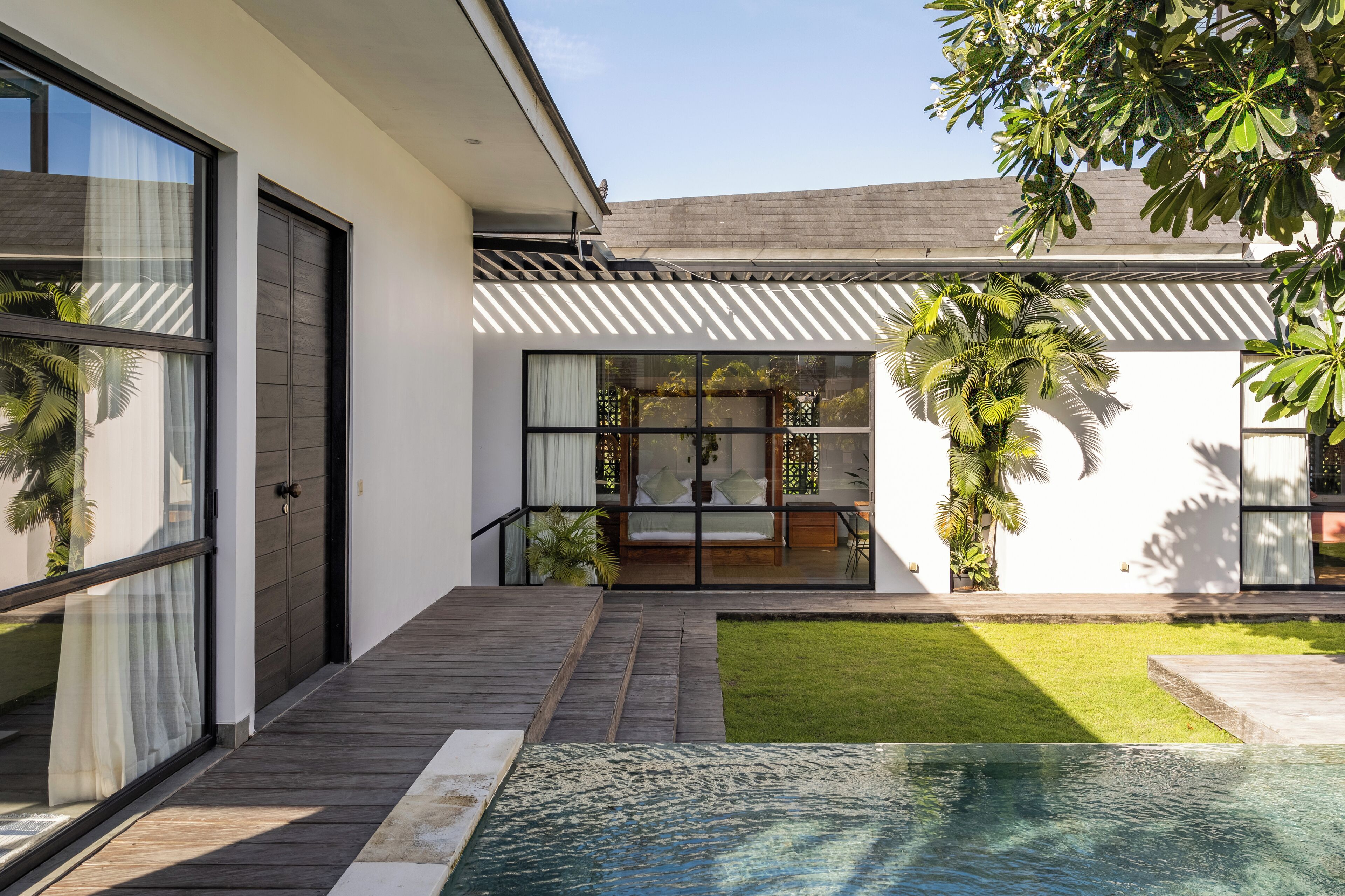 Une maison moderne dotée d’une grande porte vitrée, d’une terrasse en bois, d’une petite piscine et d’une pelouse bien entretenue.