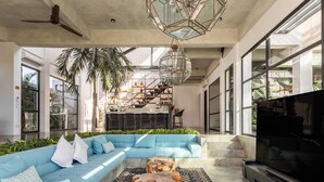 A modern living room with a sectional sofa, a flat-screen TV, and a staircase leading to a balcony. - Smeralda Villa (Canggu)