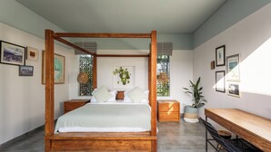 A bedroom with a four-poster bed, a wooden desk, and a chair. There are framed pictures on the walls and a potted plant on the desk. - Smeralda Villa (Canggu)