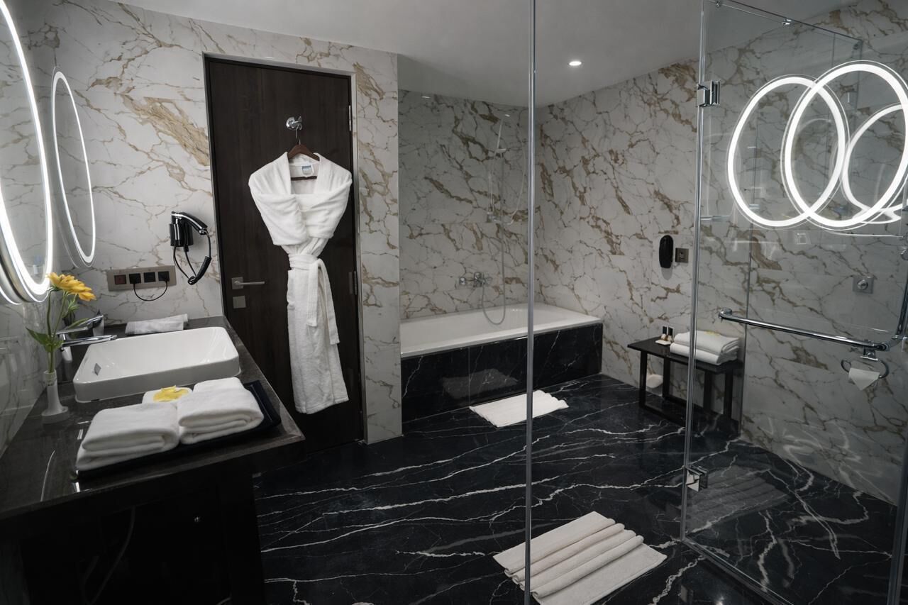 Ein modernes Badezimmer mit Marmorboden, einem Waschtisch inklusive Spiegel, einer Badewanne und einer Duschkabine aus Glas.