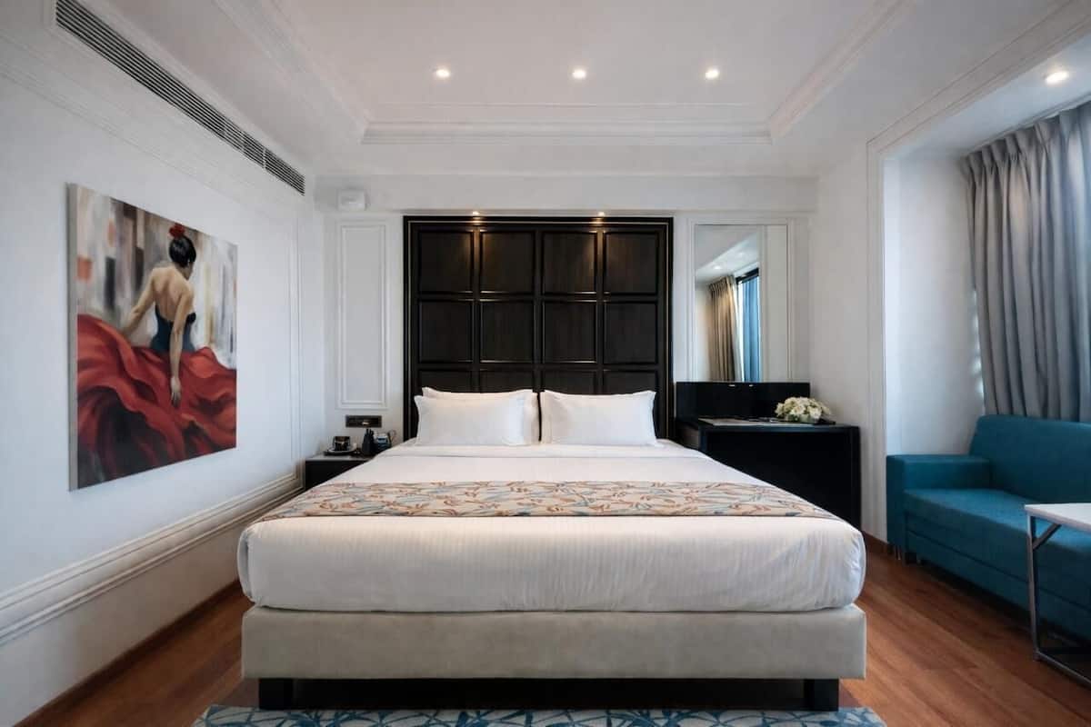 Een ruime slaapkamer met een groot bed, een donker hoofdbord, een nachtkastje, een blauwe bank en een schilderij aan de muur.