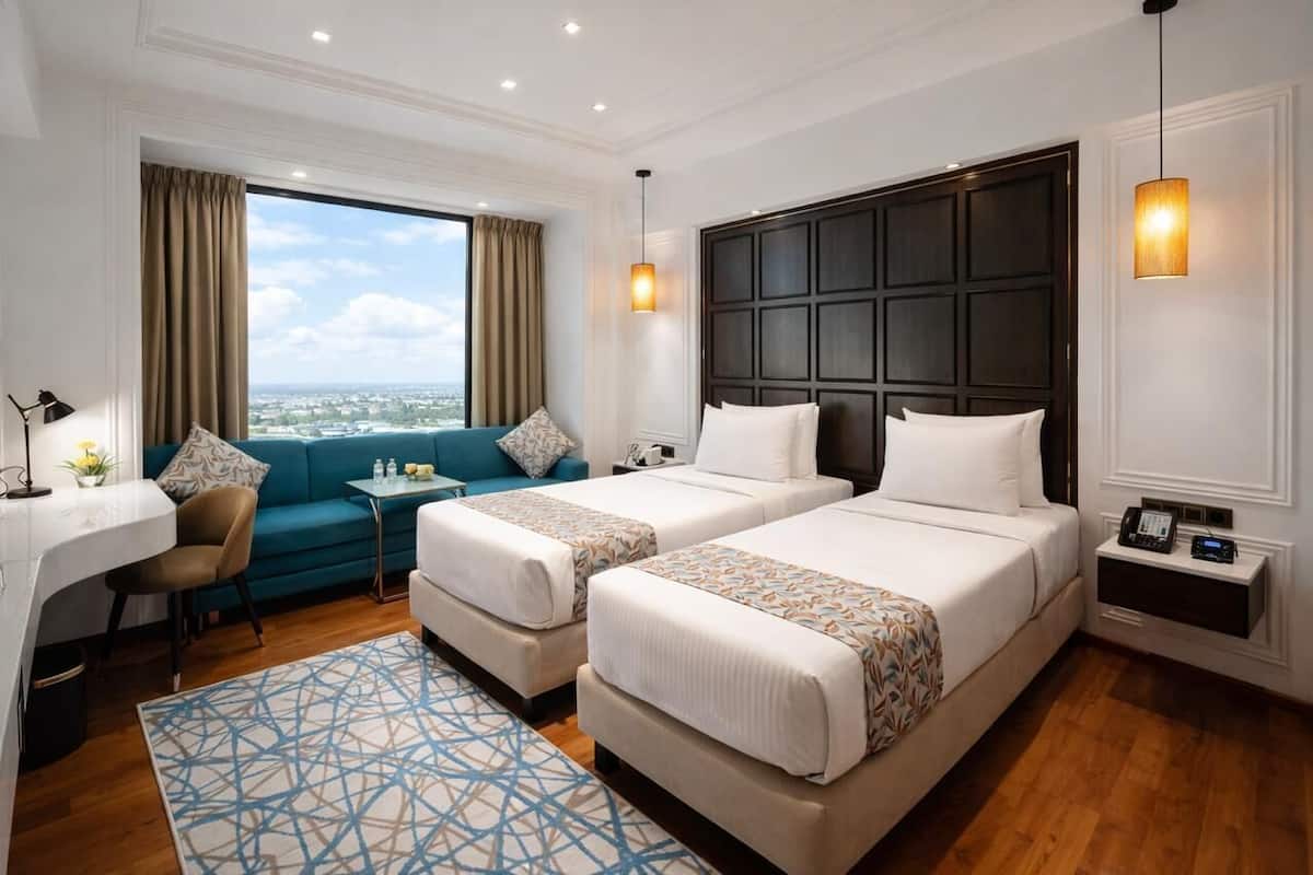 Een hotelkamer met twee bedden, een bank, een bureau en uitzicht op de stad.