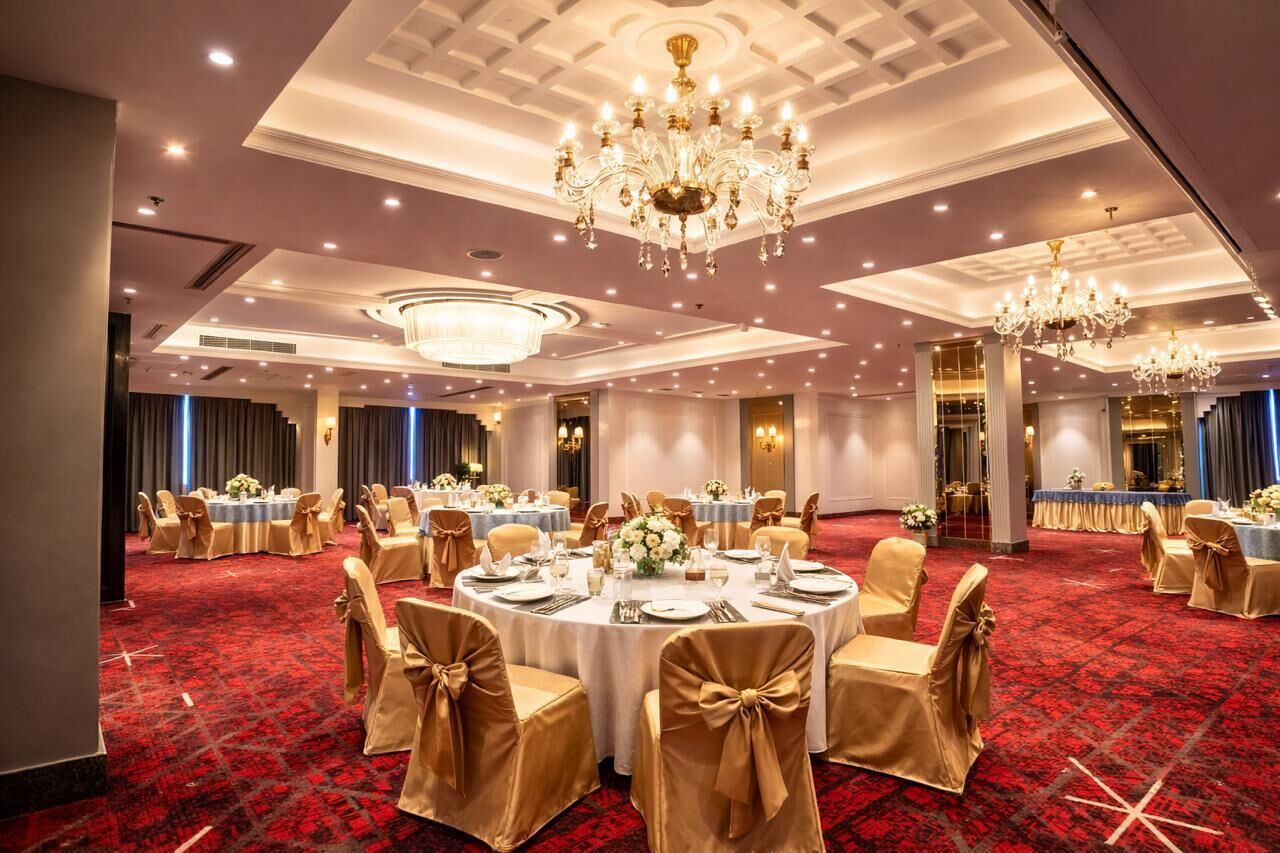 A banquet hall with round tables, gold chairs, and chandeliers.